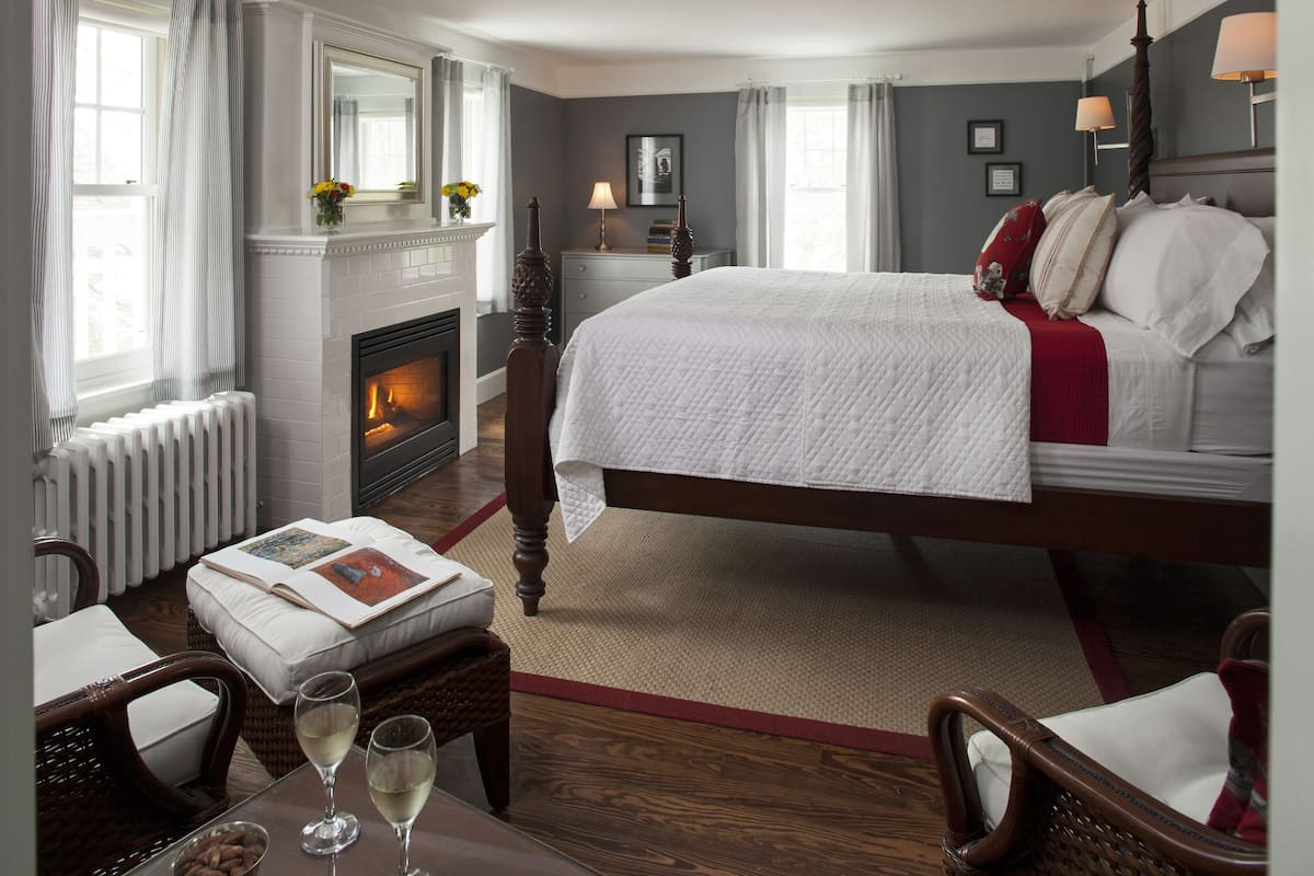 A bedroom with a large bed, a fireplace, a nightstand, and a window with curtains.