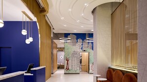 Un hall d’hôtel moderne avec un comptoir d’accueil bleu, un espace salon et une fresque représentant un paysage urbain.