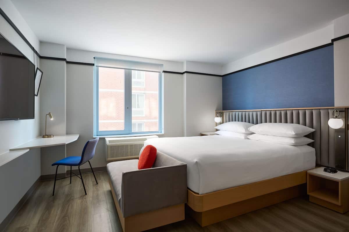 A modern hotel room with a large bed, a desk, and a chair.
