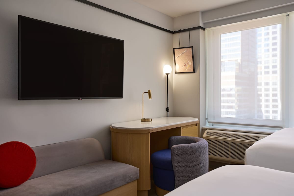A hotel room with a flat-screen TV, a desk with a lamp, a sofa, and a bed.