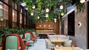 Un espace de restauration intérieur moderne, avec des chaises rembourrées de couleur verte et rouge, des tables en bois et des plantes suspendues.