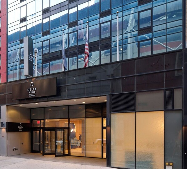 A modern hotel entrance with a glass facade, a prominent sign for Delta Hotels, and flags outside.