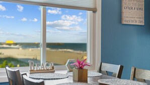 Un espace repas avec vue sur la plage, un panneau en bois sur lequel est écrit le mot « PLAGE », et une citation encadrée accrochée au mur.