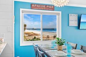 Un comedor con vistas a la playa, un letrero que dice "APACHE PIER 1206 FEET LONGEST PIER ON THE EAST COAST", y un adorno de pared con motivos playeros.