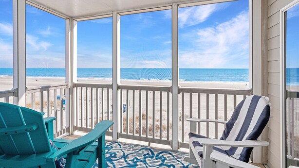 Un balcon abrité offrant une vue sur la plage, deux chaises et un tapis à motifs.