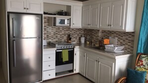 Una cocina compacta con armarios blancos, un refrigerador de acero inoxidable, un microondas y una estufa.