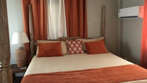 Un dormitorio con cama, cortinas naranjas, cabecero de madera, mesita de noche con lámpara y equipo de aire acondicionado.