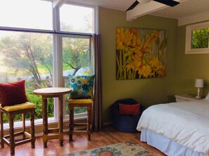 Una camera da letto con un letto, una finestra, una sedia, un tavolino e un quadro.
