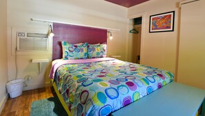 A bedroom with a colorful bedspread, a bedside table, a wall-mounted heater, and a small trash bin. - Kokopelli Lodge (Moab)
