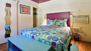 A bedroom with a bed, a bedside table, a mirror, a wall-mounted air conditioner, and a colorful abstract painting. - Kokopelli Lodge (Moab)