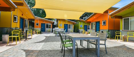 A covered outdoor seating area with tables and chairs, surrounded by colorful buildings with doors and windows.