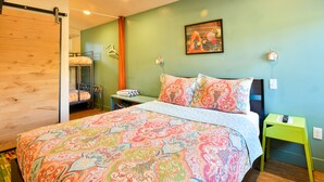 Une chambre à coucher avec un lit, un mur vert, un tableau, une table de chevet et un porte-vêtements suspendu.