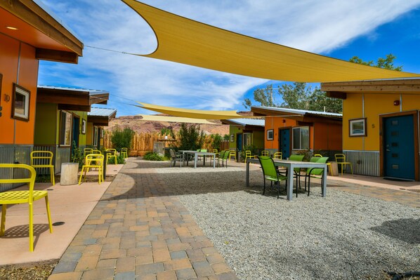 A courtyard with outdoor seating, a gravel path, and buildings with doors and windows.