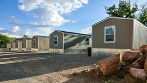 A row of single-story mobile homes with a gravel driveway and large rocks in the foreground. - Red Sands Habitation (Moab)