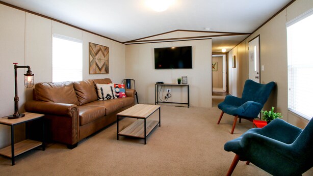 A living room with a brown leather sofa, a wooden coffee table, a blue armchair, a small side table with a lamp, and a flat-screen TV mounted on the wall. - Red Sands Habitation (Moab)