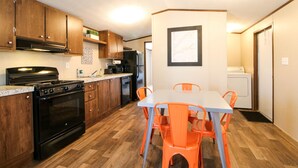A modern kitchen with wooden cabinets, a black stove, and a dining table with orange chairs. - Red Sands Habitation (Moab)