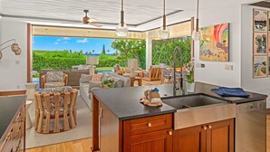 Una cocina moderna con una isla grande, armarios de madera y vistas a un jardín exuberante y una piscina.