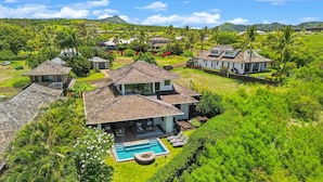 Una casa grande con piscina, rodeada de vegetación exuberante y palmeras.
