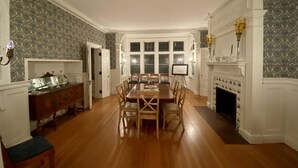 A dining room with a wooden table and chairs, a fireplace, and patterned wallpaper. - Beautiful, large, historic 6 bedroom home.   (Oswego)