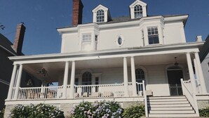 A two-story white house with a front porch, a chimney, and a small balcony. - Beautiful, large, historic 6 bedroom home.   (Oswego)