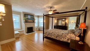 A four-poster bed with a patterned bedspread, a fireplace, a ceiling fan, and a view of the outside through a window. - Beautiful, large, historic 6 bedroom home.   (Oswego)