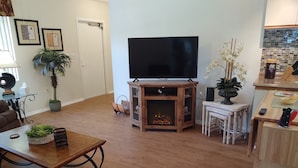 Ein Wohnzimmer mit Kamin, Fernseher, Esstisch und Küchenzeile.