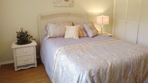 Ein Schlafzimmer mit einem Rattan-Kopfstück, einem Bett mit gemustertem Überwurf, einem Nachttisch mit Lampe und einem Wandbild.