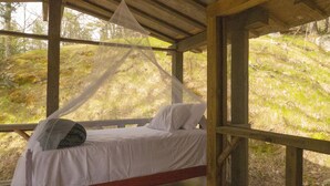 Ein Bett mit Baldachin in einer Holzhütte mit Blick auf einen bewaldeten Hang.
