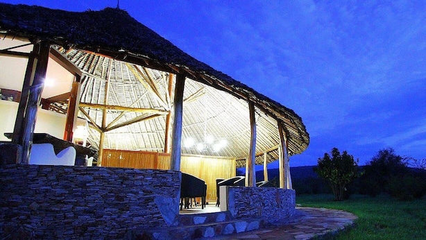 A thatched-roof building with a stone foundation, a covered outdoor seating area, and a view of the surrounding landscape.