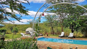 A pool area with lounge chairs, a hot tub, and a pergola with a swing.