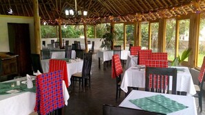 An outdoor dining area with tables and chairs, covered by a wooden roof with string lights.