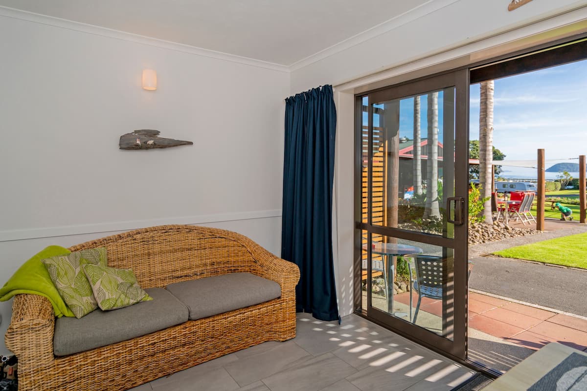 A wicker sofa with cushions, a glass door leading outside, and a small table with chairs.