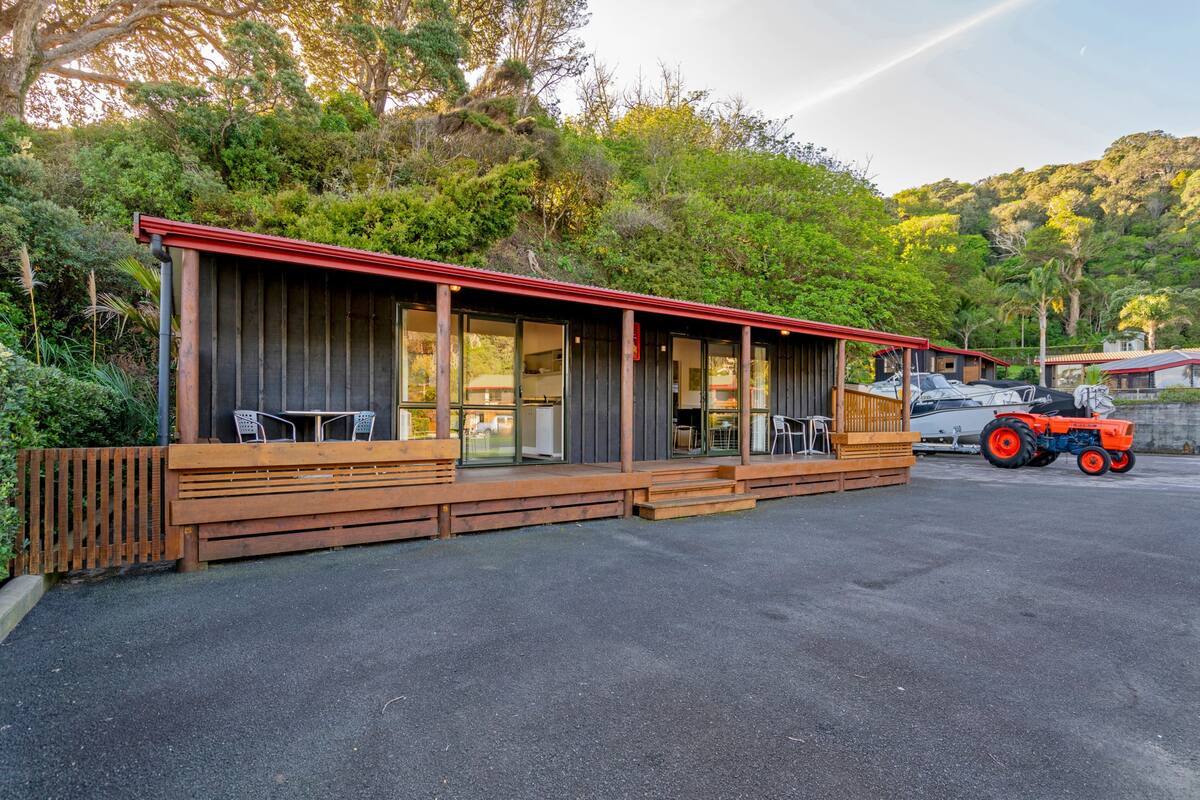 A wooden building with a red roof, large windows, and a covered outdoor seating area.