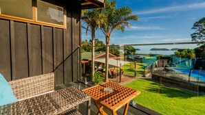 Un balcón con mobiliario de mimbre, una mesa de madera y vistas a una piscina y islas en la distancia.