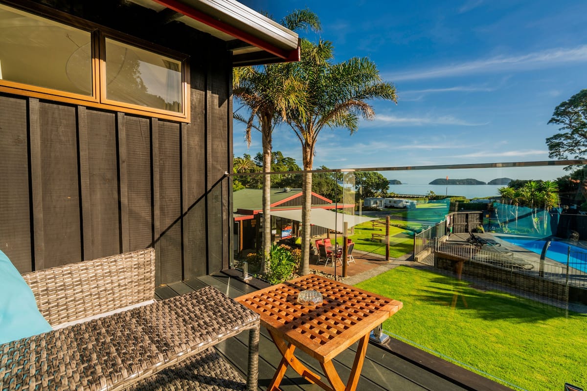 A balcony with wicker furniture, a wooden table, and a view of a swimming pool and distant islands.