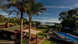 Zona de piscina con un espacio de estar techado, vistas al mar y un césped cuidado.