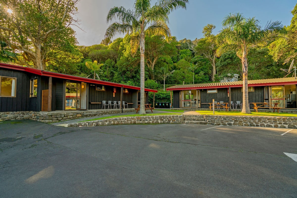 A building with two sections, each with a red roof and surrounded by trees.