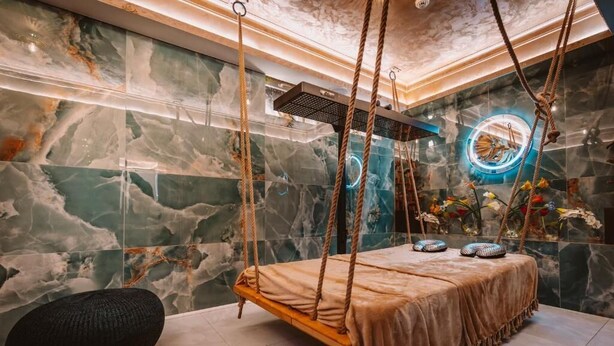 Un espace de détente moderne avec un lit suspendu en bois, des murs en marbre et une décoration circulaire illuminée par des néons.
