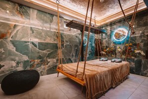 Un moderno cuarto de spa con una hamaca de madera, paredes de mármol y un adorno circular iluminado con neón.