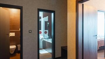 A modern hotel room with a wooden floor, a visible bathroom with a toilet and sink, and a bed with a pink blanket.