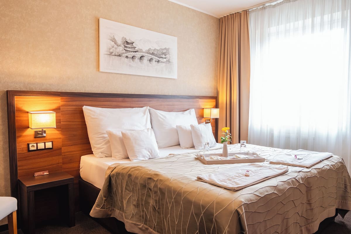 Ein Hotelzimmer mit einem großen Bett, zwei Nachttischlampen, einem Nachttisch, einer Ablage mit Toilettenartikeln und einem Gemälde an der Wand.