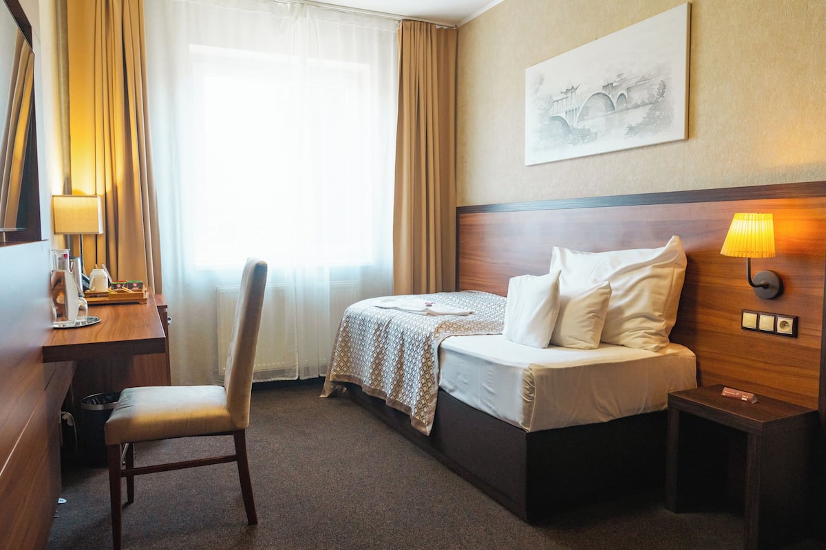 Ein Hotelzimmer mit Bett, Schreibtisch, Stuhl, Nachttisch und einem Fenster mit Vorhängen.