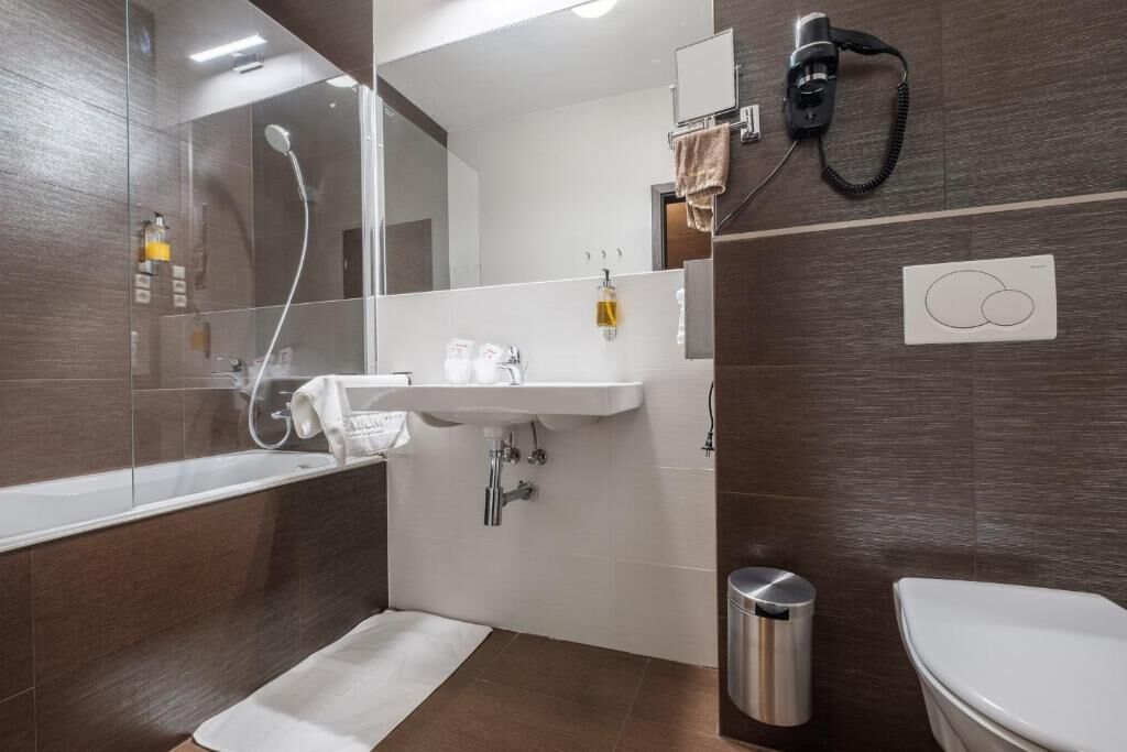 Un baño moderno con cabina de ducha de vidrio, un lavabo blanco, inodoro y secador de pelo en la pared.