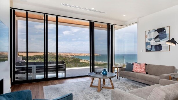 Amplia sala de estar con un gran ventanal corredera que da a un balcón y ofrece vistas panorámicas del mar y los acantilados.