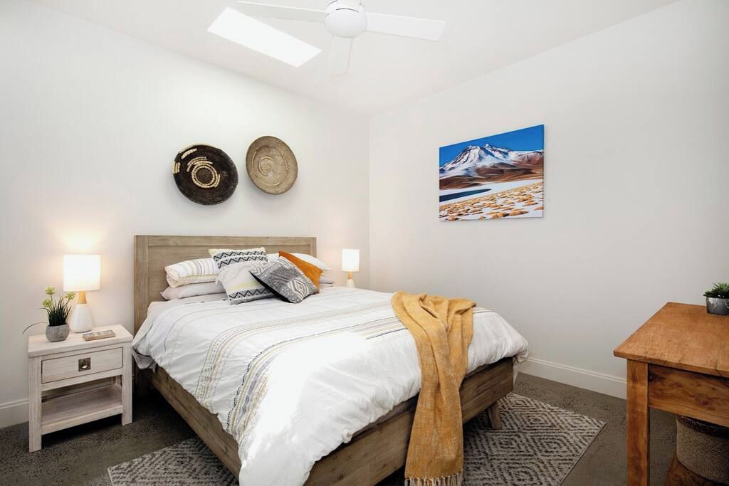A bedroom with a bed, bedside tables, a ceiling fan, a wall-mounted picture, and a small table with a plant.