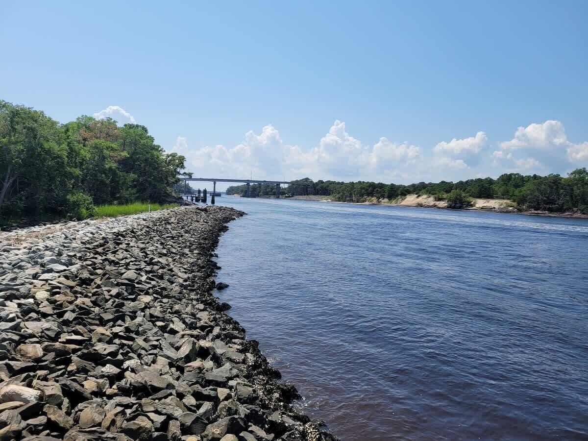 Une rive avec un littoral rocheux, un pont au loin et un ciel dégagé.