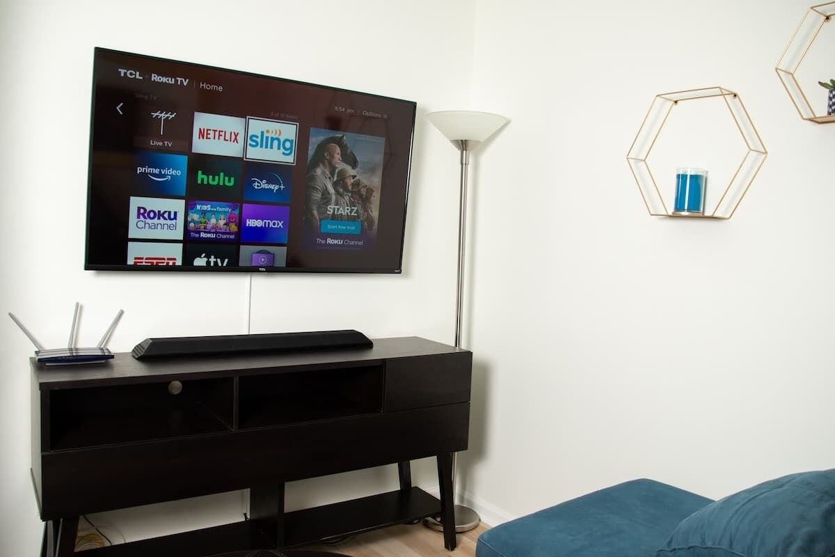Moderni olohuone, jossa seinälle on asennettu litteänäyttöinen televisio, josta näkyvät erilaiset suoratoistopalvelut. Huoneessa on myös musta viihdekeskus, lattiavalaisin ja kuusikulmainen hylly, jossa on lasinen säilytysastia.
