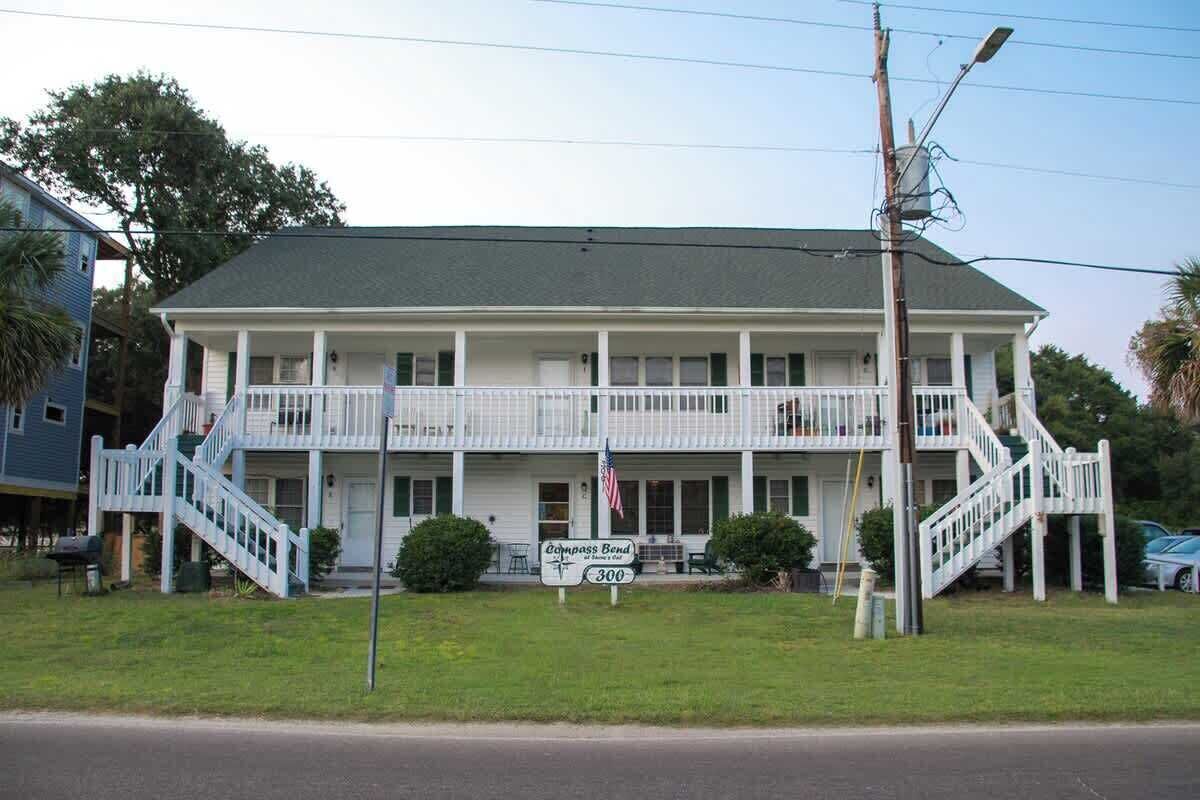 A two-story building with a porch, a sign indicating 'Compass Bend 300,' and a flagpole with an American flag.