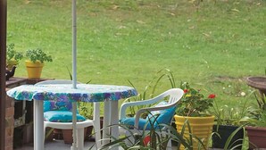 An outdoor patio area with a round table and two chairs, surrounded by potted plants. - Welcome to your Home away from Home. Pacific Studio offers everything to make your stay comfortable (Nambucca Heads)