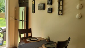 A dining area with a table set for two, a refrigerator, and wall decorations including a clock and humorous signs. - Cozy Cabin In Roselle (Roselle)
